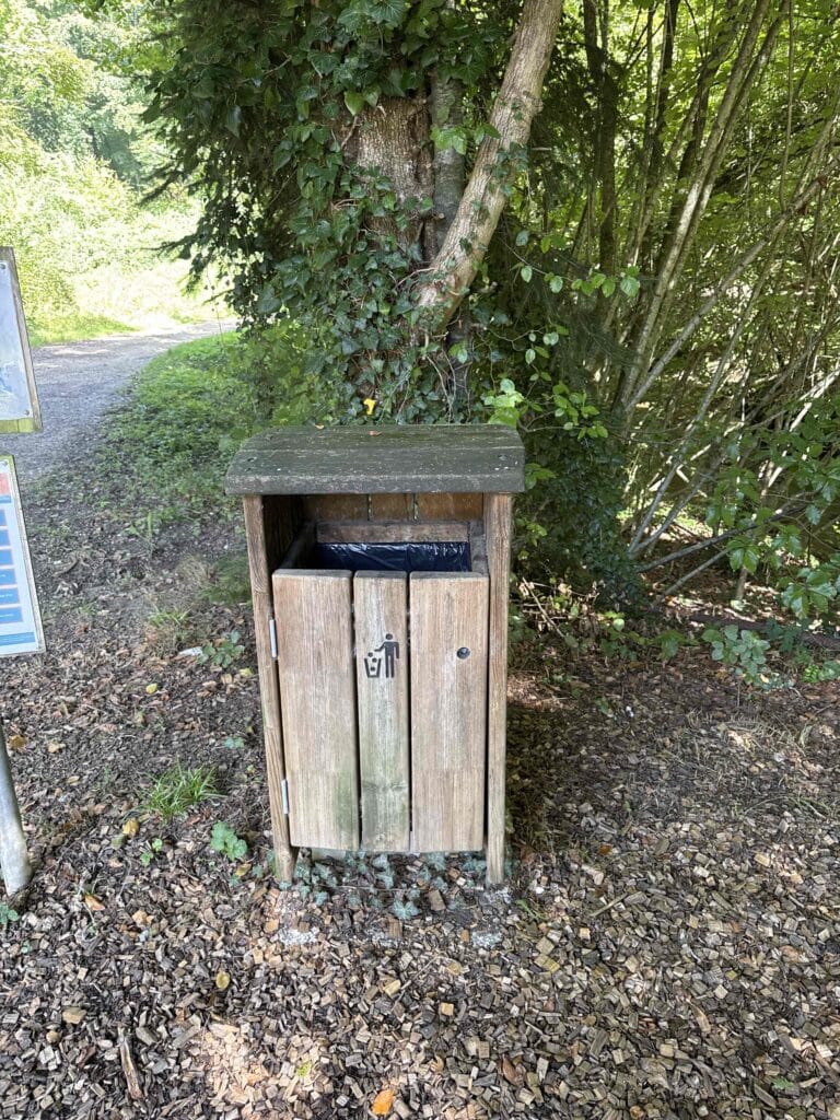 Poubelle en bois dans un chemin boisé.