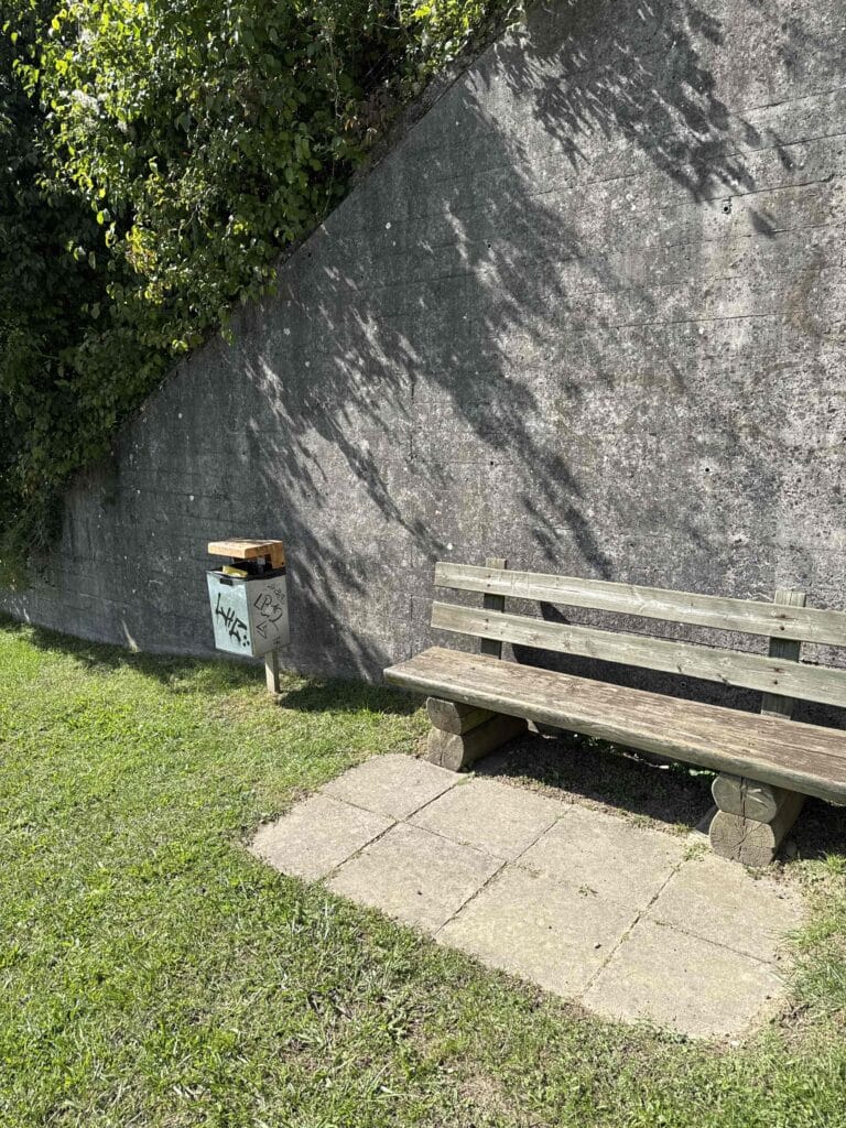 Banc en bois près d'un mur avec poubelle.